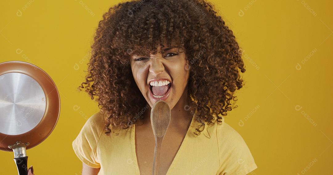 mulher de cabelo encaracolado jovem linda com panela e colher nas mãos querendo cozinhar