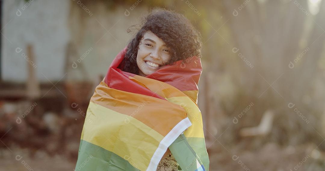 Mulher jovem de cabelo encaracolado cobrindo com a bandeira do orgulho lgbt