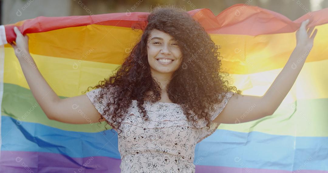 Mulher jovem de cabelo encaracolado cobrindo com bandeira do orgulho lgbt