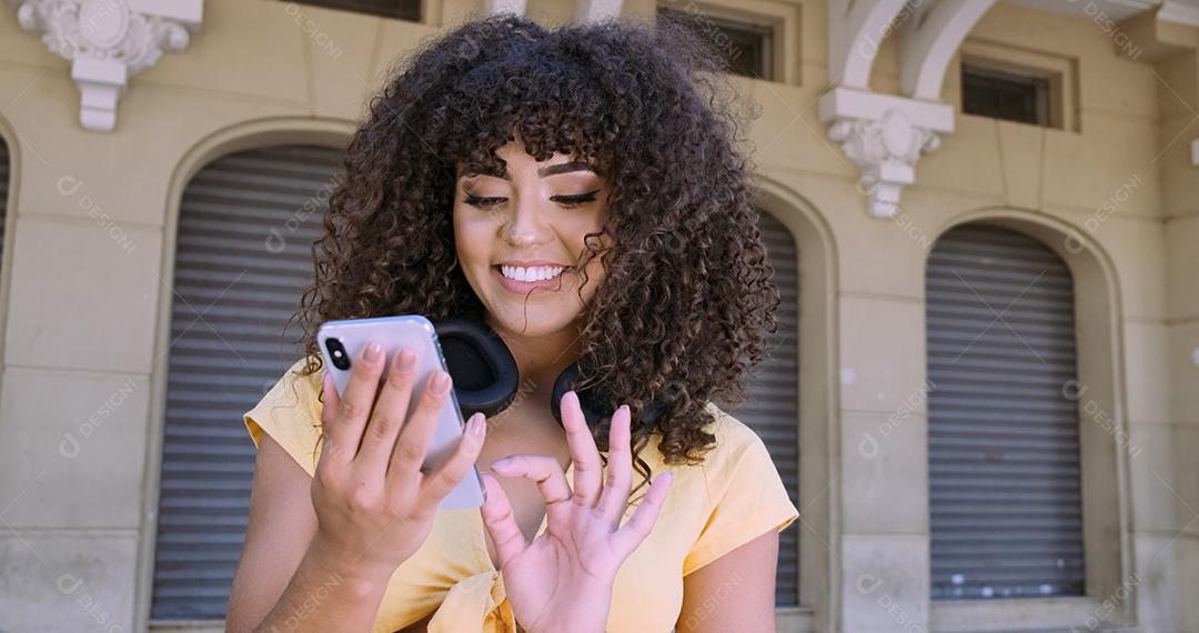 Jovem negra de cabelo encaracolado andando usando o celular. Mensagens de texto