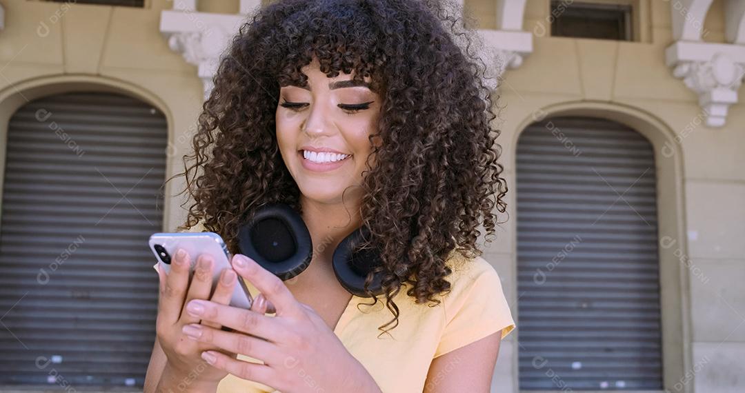 Jovem negra de cabelo encaracolado andando usando o celular. Mensagens de texto