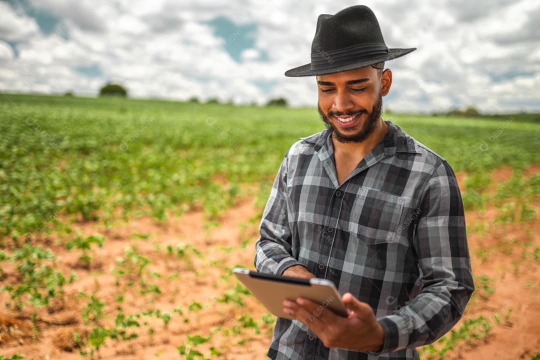 Agricultor latino-americano trabalhando na plantação de soja, examinando o desenvolvimento da cultura no tablet.