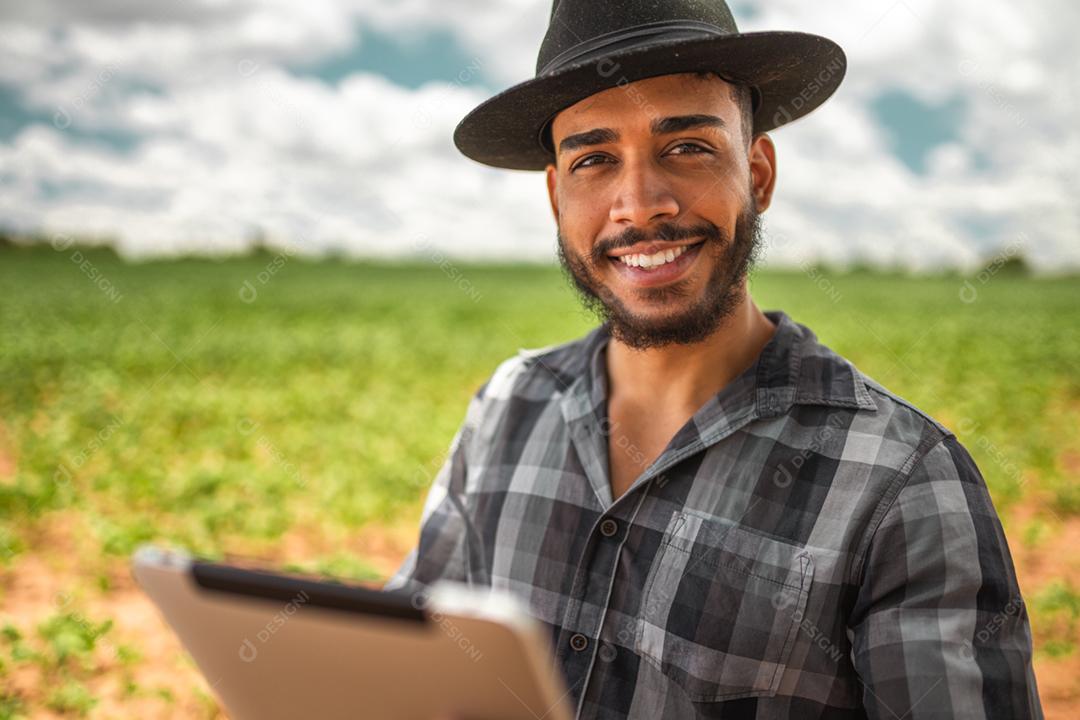 Agricultor latino-americano trabalhando na plantação de soja, examinando o desenvolvimento da cultura no tablet.