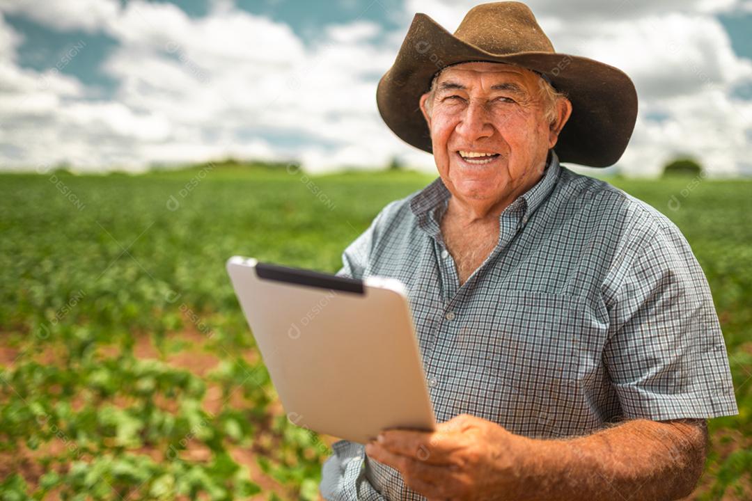 Agricultor latino-americano trabalhando na plantação de soja, examinando o desenvolvimento da cultura no tablet