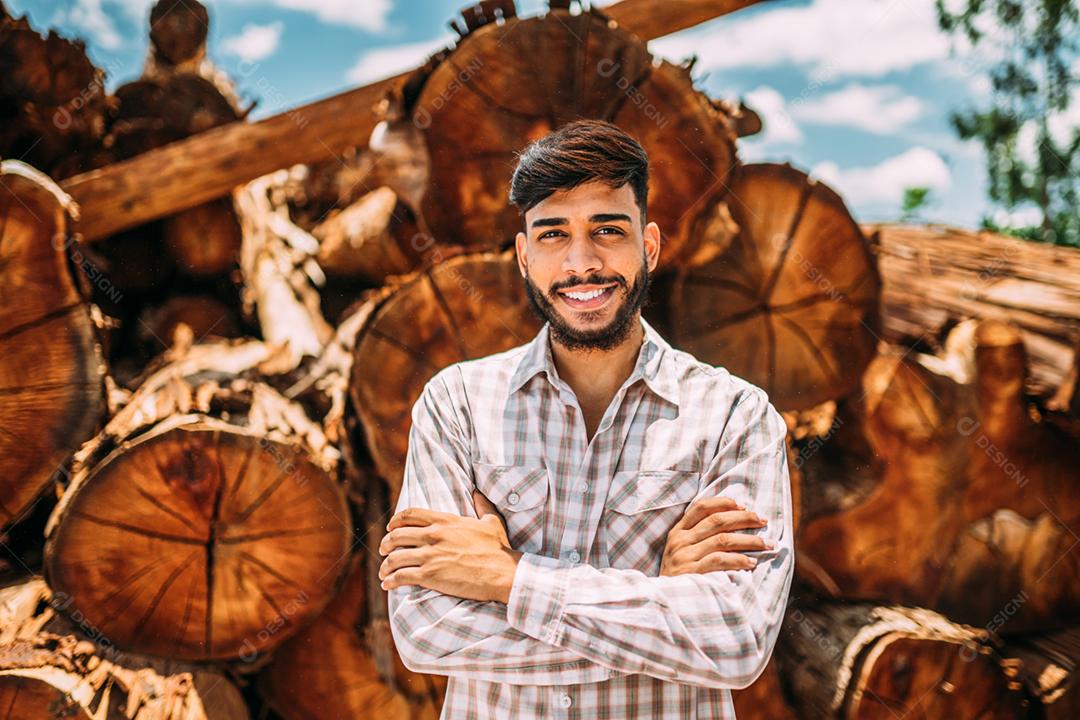 Retrato de jovem latino trabalhando ao lado de troncos de árvores.