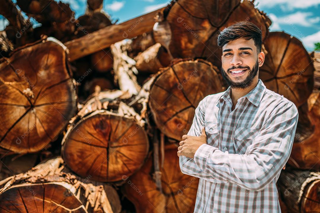 Retrato de jovem latino trabalhando ao lado de troncos de árvores.
