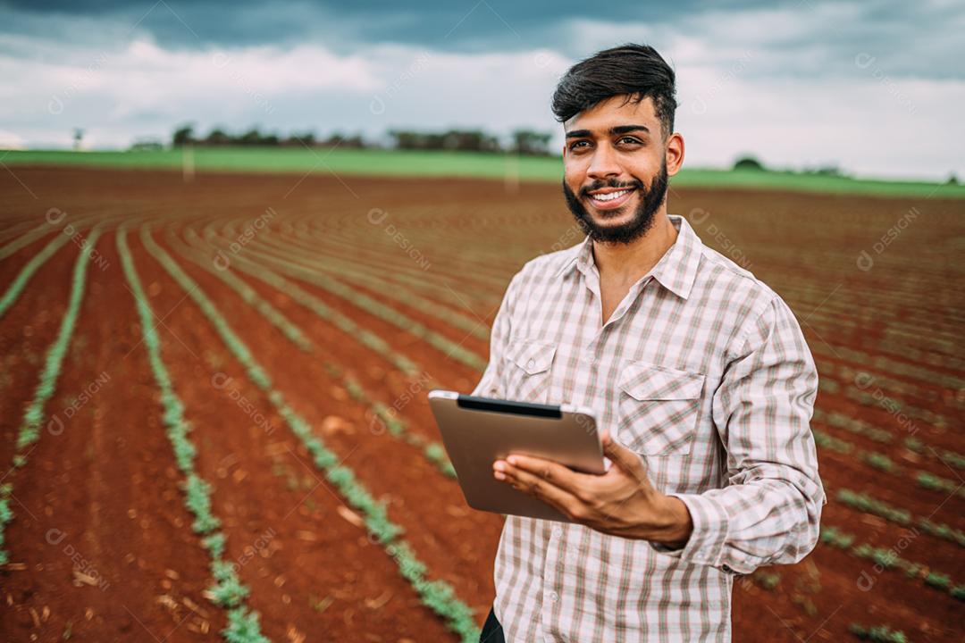 Jovem agricultor latino trabalhando com tablet digital na plantação de amendoim. Agricultor brasileiro olhando para a câmera.
