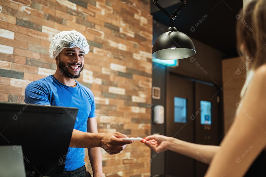 Balconista latina com um boné na cabeça anotando o pedido de uma cliente.