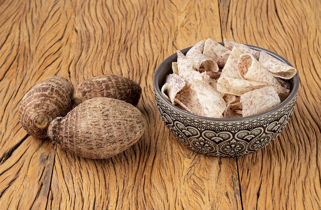 Chips de inhame ou taro em uma tigela com vegetais crus sobre a mesa de madeira