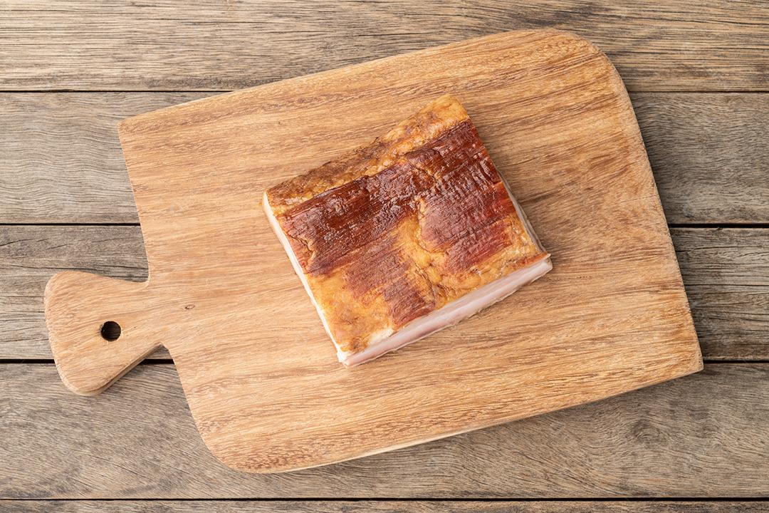 Pedaço de bacon defumado sobre tábua de madeira