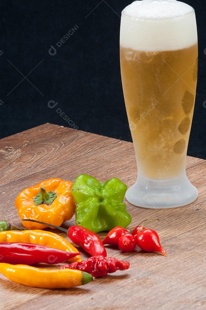Pimentas variadas sobre mesa de madeira acompanhado com cerveja gelada. Pano de fundo alimentar