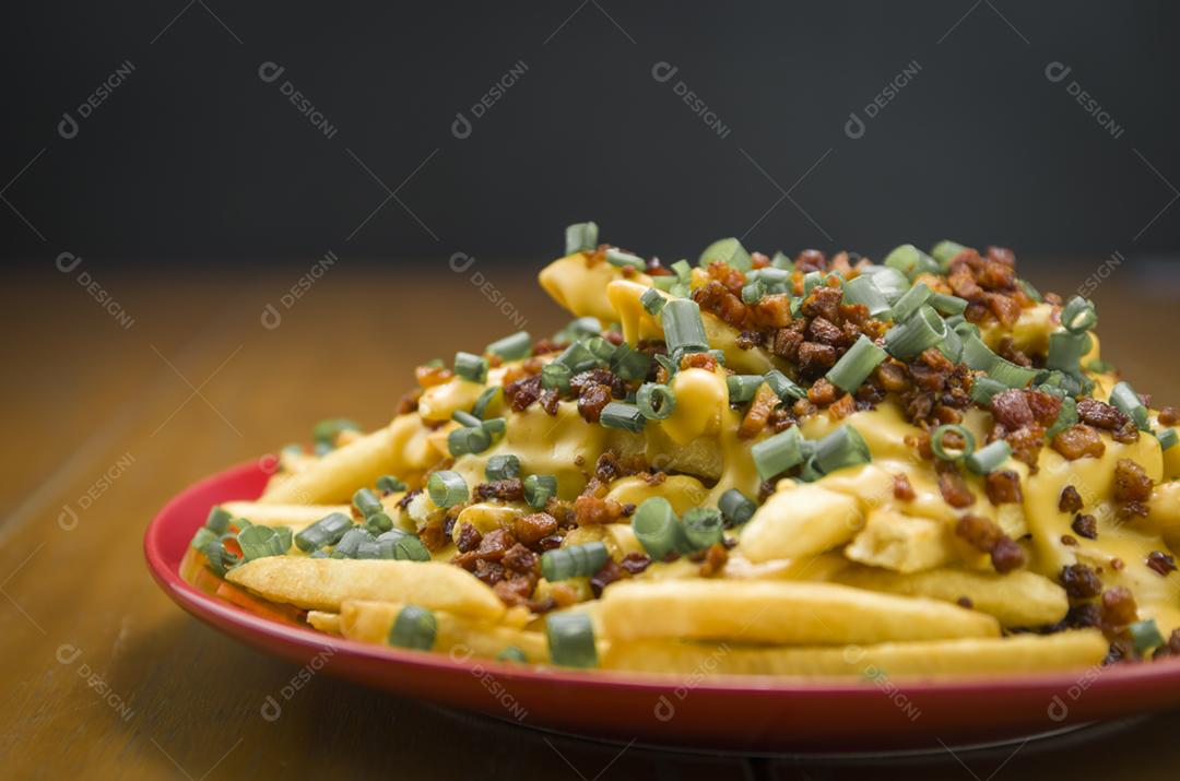 Saborosas batatas fritas, cheddar e bacon close-up em fundo de madeira e preto