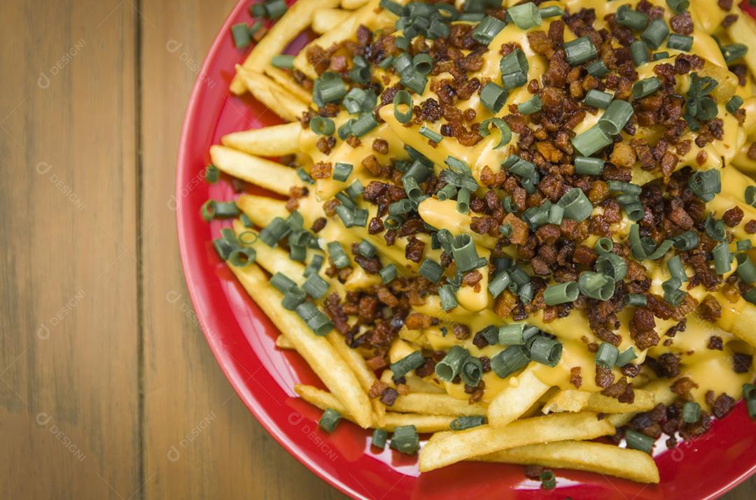 Saborosas batatas fritas, cheddar e bacon close-up em fundo de madeira e preto