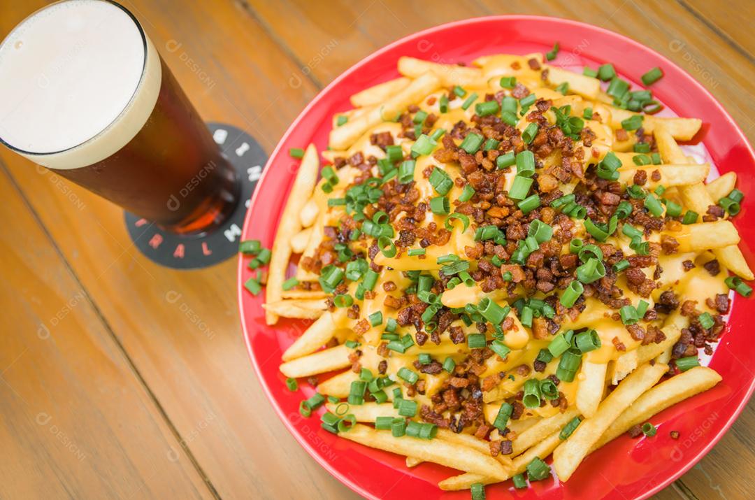 Saboroso close-up de batatas fritas, cheddar e bacon, cerveja em fundo de madeira e preto