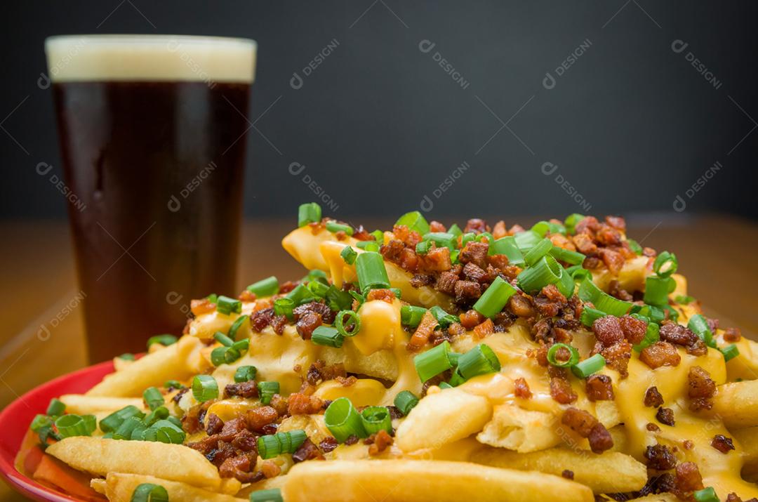 Saboroso close-up de batatas fritas, cheddar e bacon, cerveja em fundo de madeira e preto