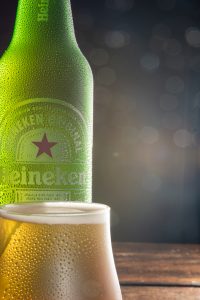 Garrafa e xícara de Heineken fotografada com fundo escuro em superfície de madeira rústica