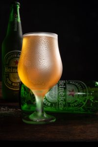 Garrafa e xícara de Heineken fotografada com fundo escuro em superfície de madeira rústica