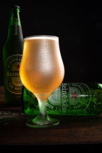Garrafa e xícara de Heineken fotografada com fundo escuro em superfície de madeira rústica