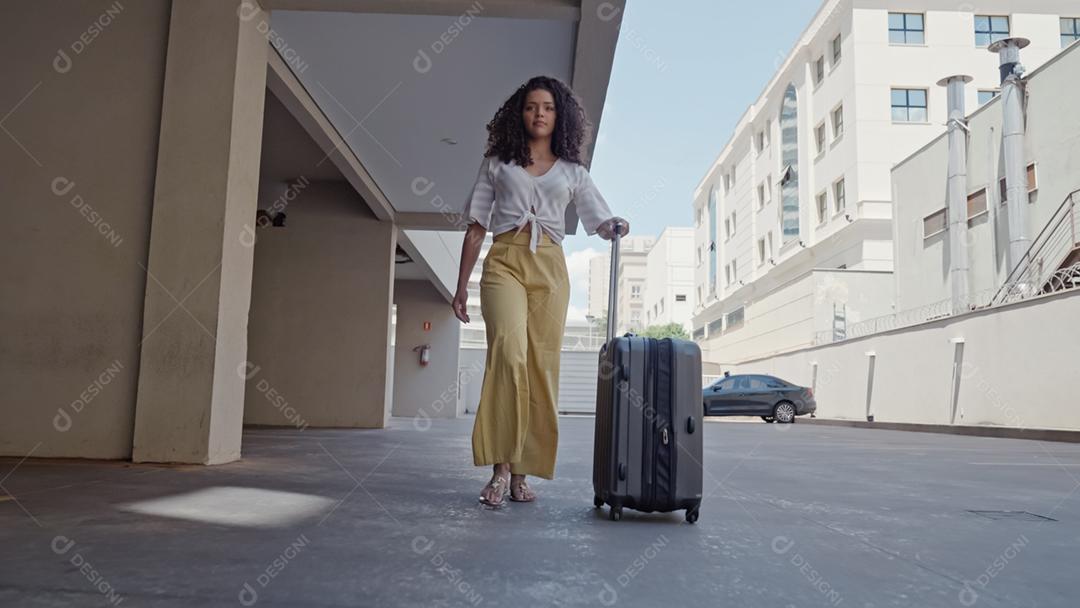 Jovem turista latina caminha com uma mala sobre rodas ao redor da cidade no fundo da garagem do hotel