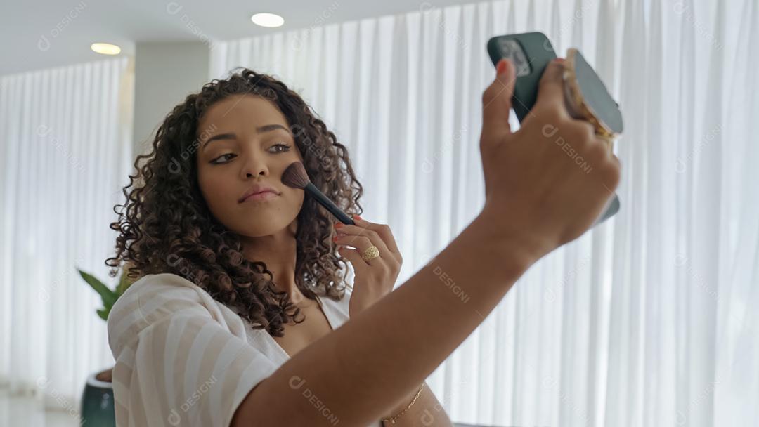 Jovem mulher latina usando seu telefone inteligente como um espelho para fazer as pazes.