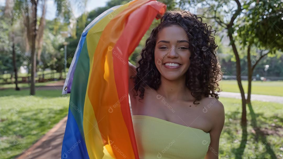 Mulher jovem de cabelo encaracolado cobrindo com a bandeira do orgulho lgbt. Mantendo o punho erguido, cobrindo a bandeira LGBT +