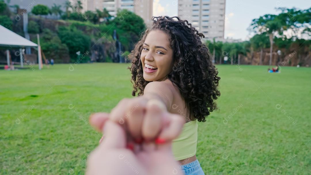 Follow me concept. Male following girlfriend holding hands in a park. POS.