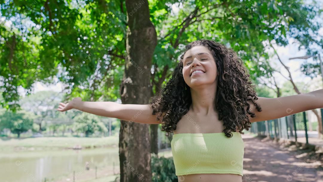 Mulher latina atraente andando no parque em um dia ensolarado e sorrindo.
