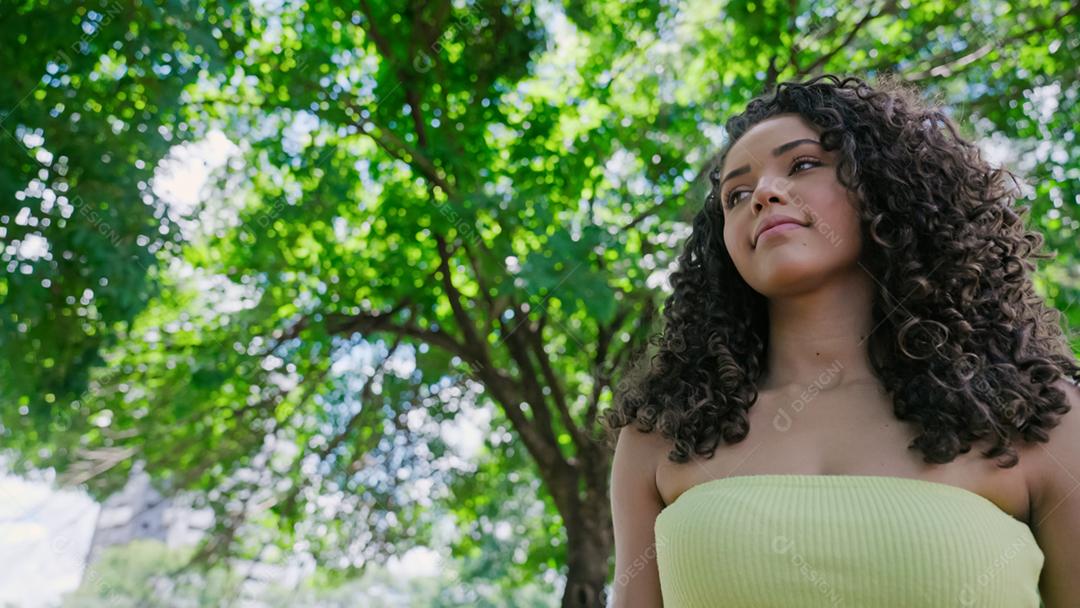 Mulher latina atraente andando no parque em um dia ensolarado e sorrindo.
