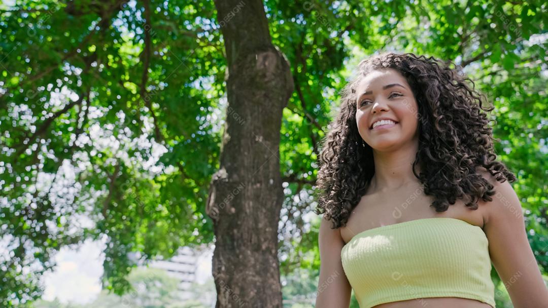 Mulher latina atraente andando no parque em um dia ensolarado e sorrindo.