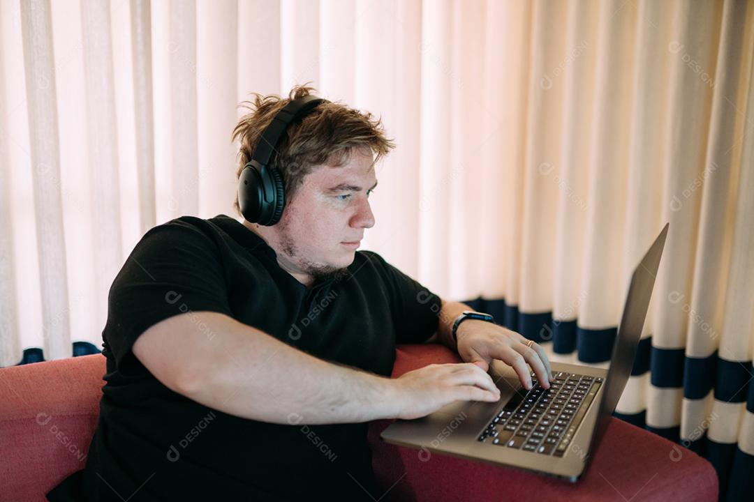 Homem concentrado sentado em casa usando computador portátil, com fones de ouvido