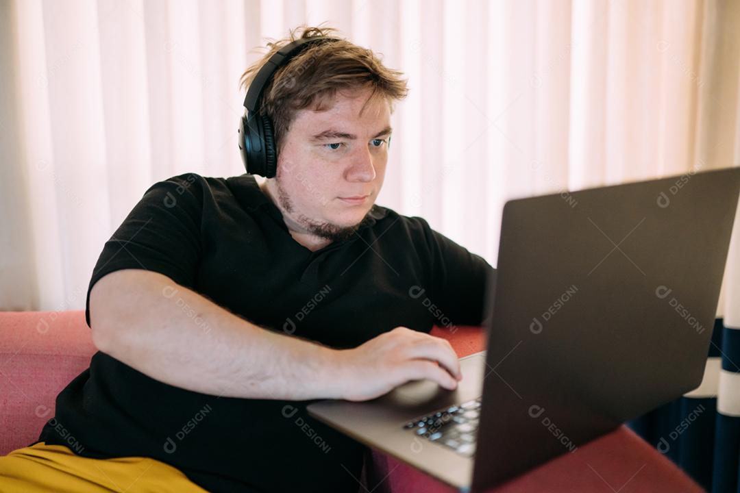 Homem concentrado sentado em casa usando computador portátil, com fones de ouvido