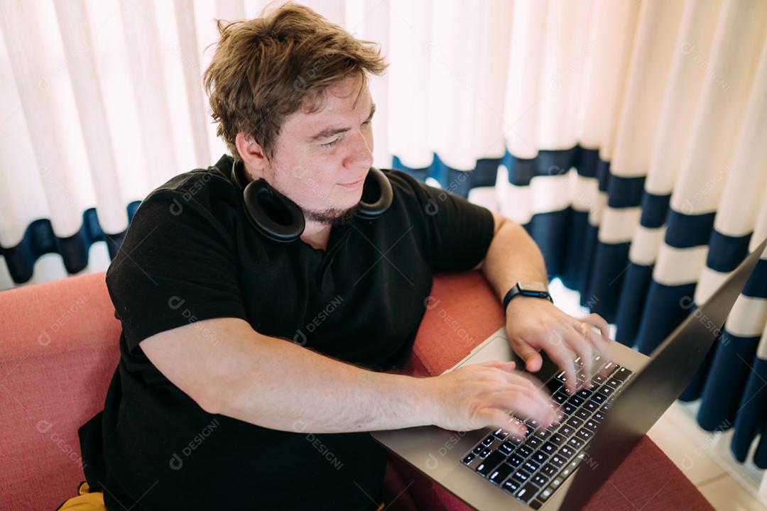 Homem concentrado sentado em casa usando computador portátil, com fones de ouvido