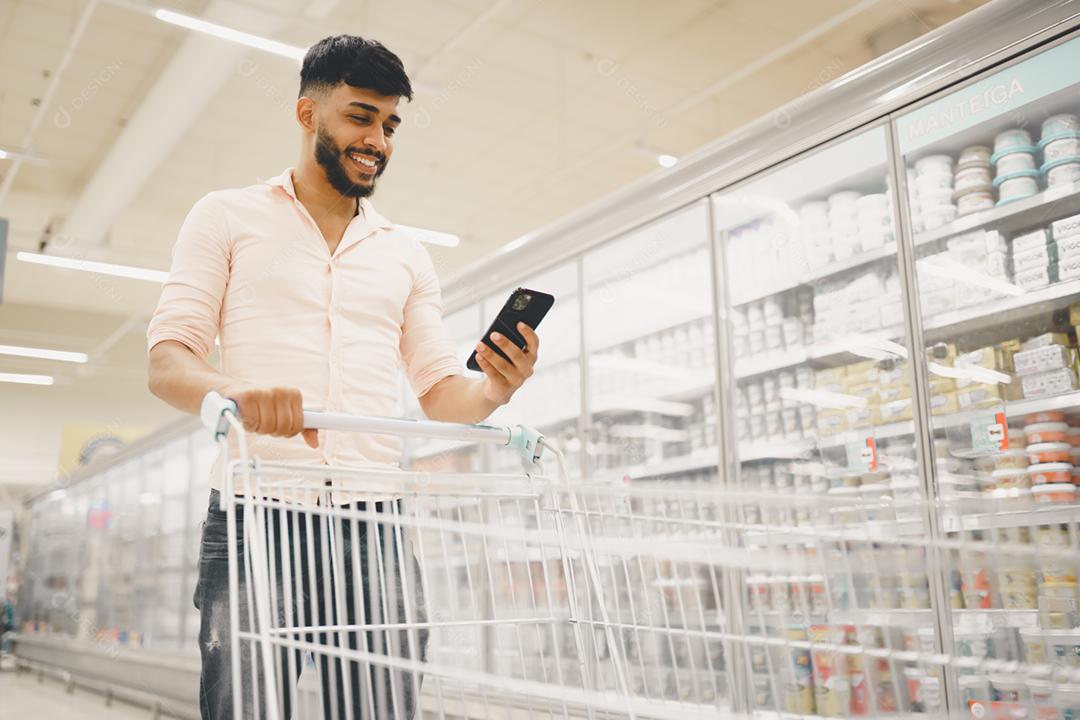 Bonito homem latino-americano usa smartphone no supermercado