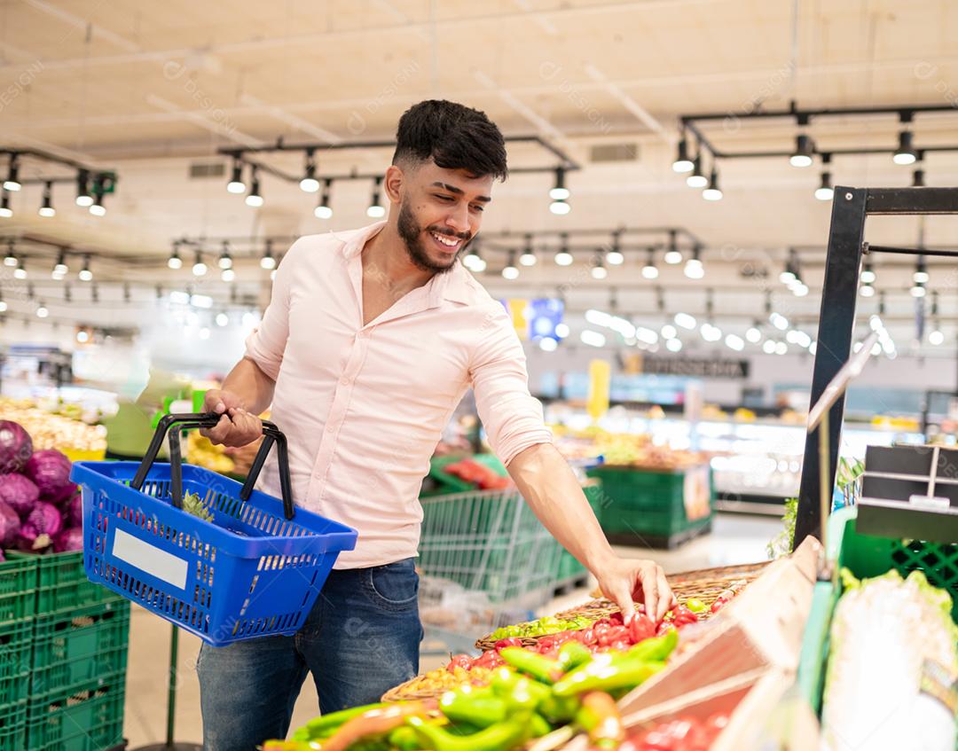 Retrato aproximado, jovem bonito da América Latina colhendo pimenta no supermercado