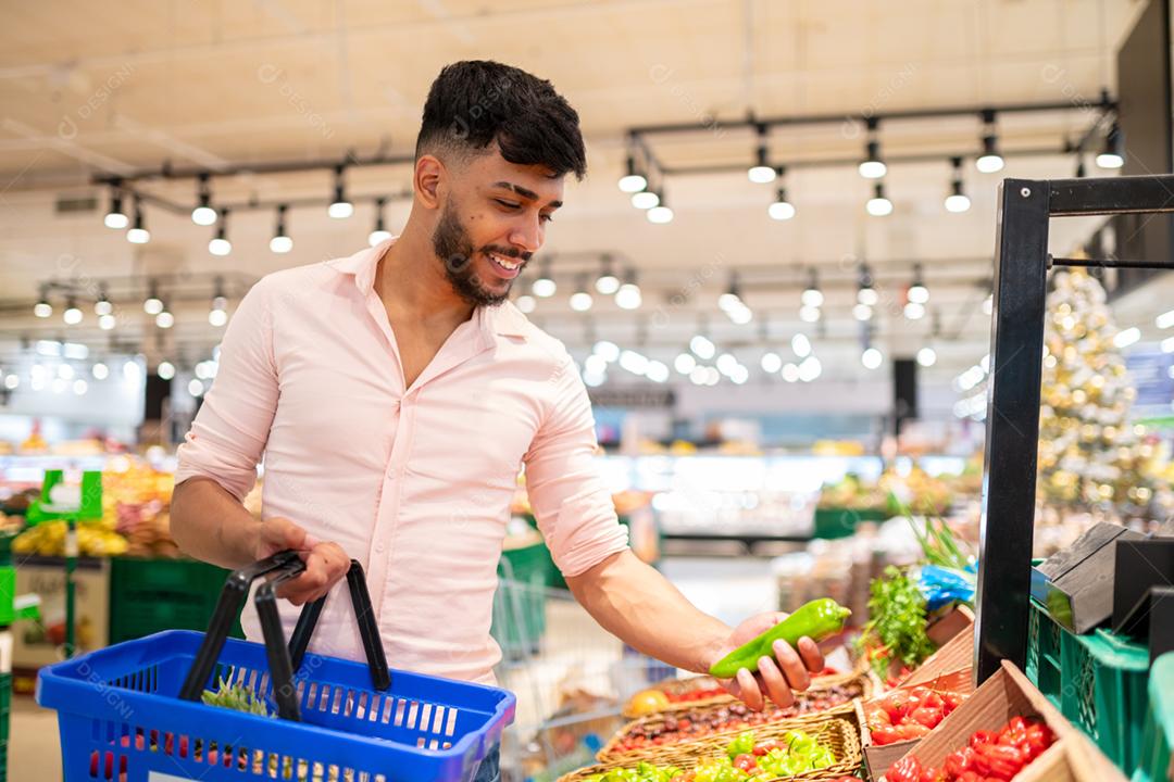 Retrato aproximado, jovem bonito da América Latina colhendo pimenta no supermercado