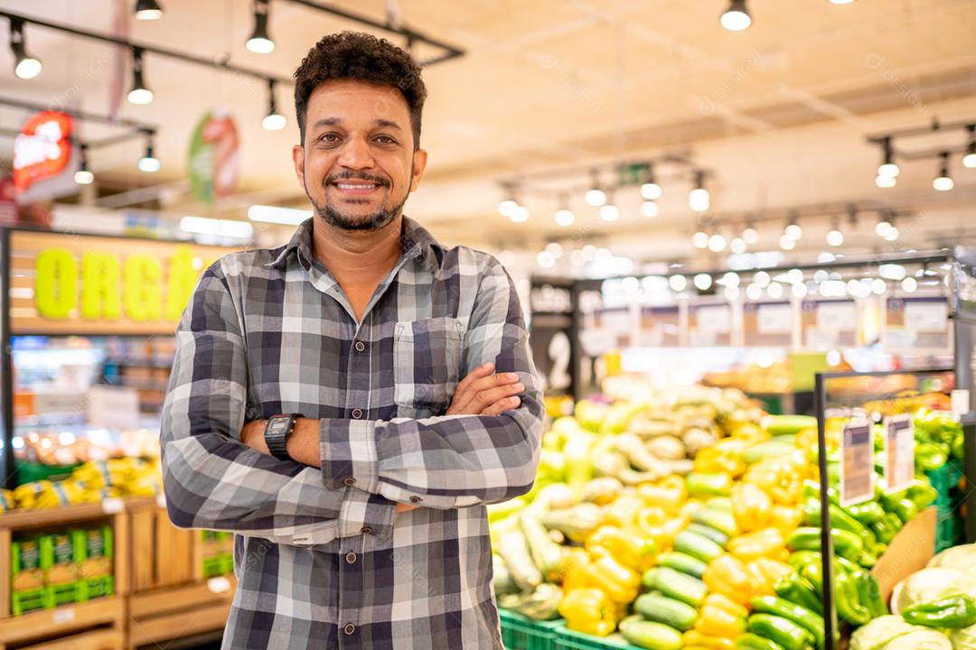 Latino-americano no supermercado. Homem sorridente com os braços cruzados e olhando para a câmera