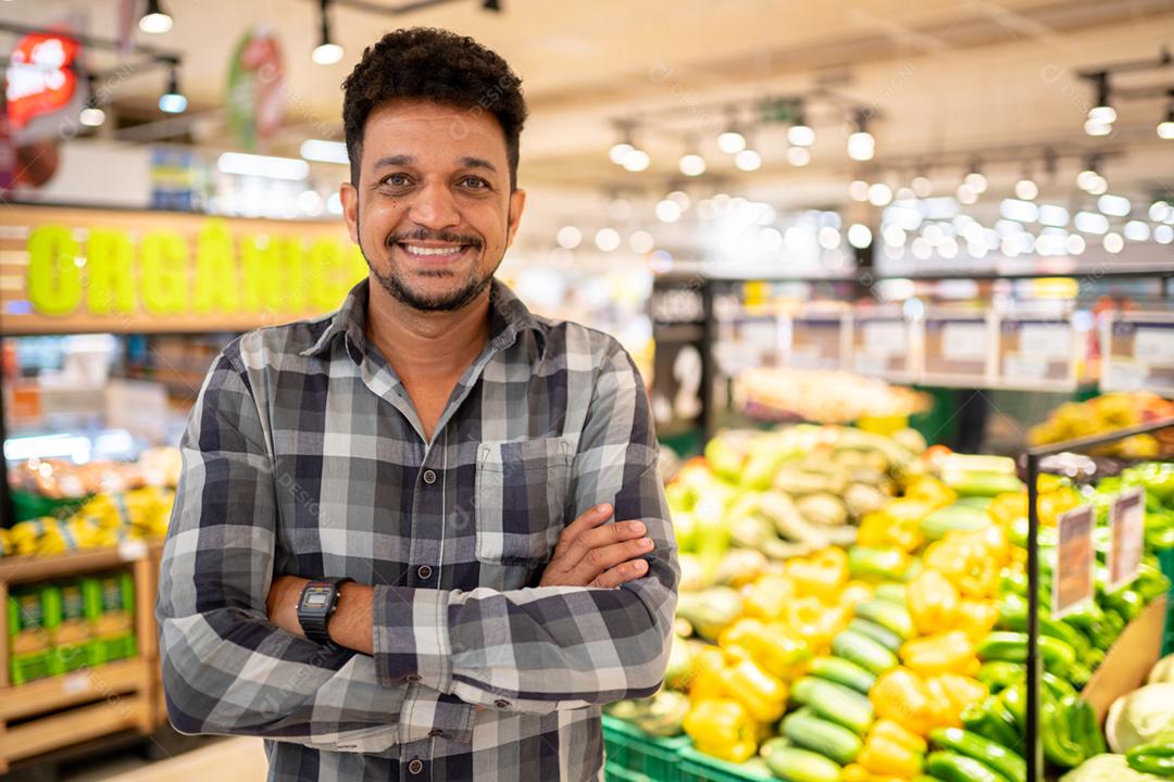 Latino-americano no supermercado. Homem sorridente com os braços cruzados e olhando para a câmera