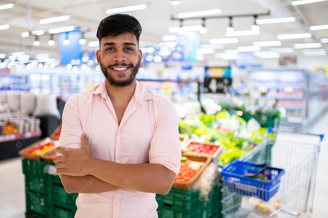 Latino-americano no supermercado. Homem sorridente com os braços cruzados e olhando para a câmera