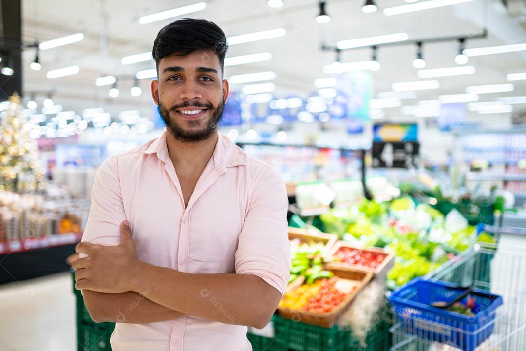 Latino-americano no supermercado. Homem sorridente com os braços cruzados e olhando para a câmera