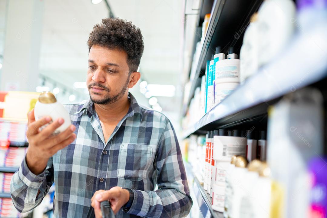 Cliente masculino latino-americano escolhendo um produto de cabelo masculino na prateleira do supermercado