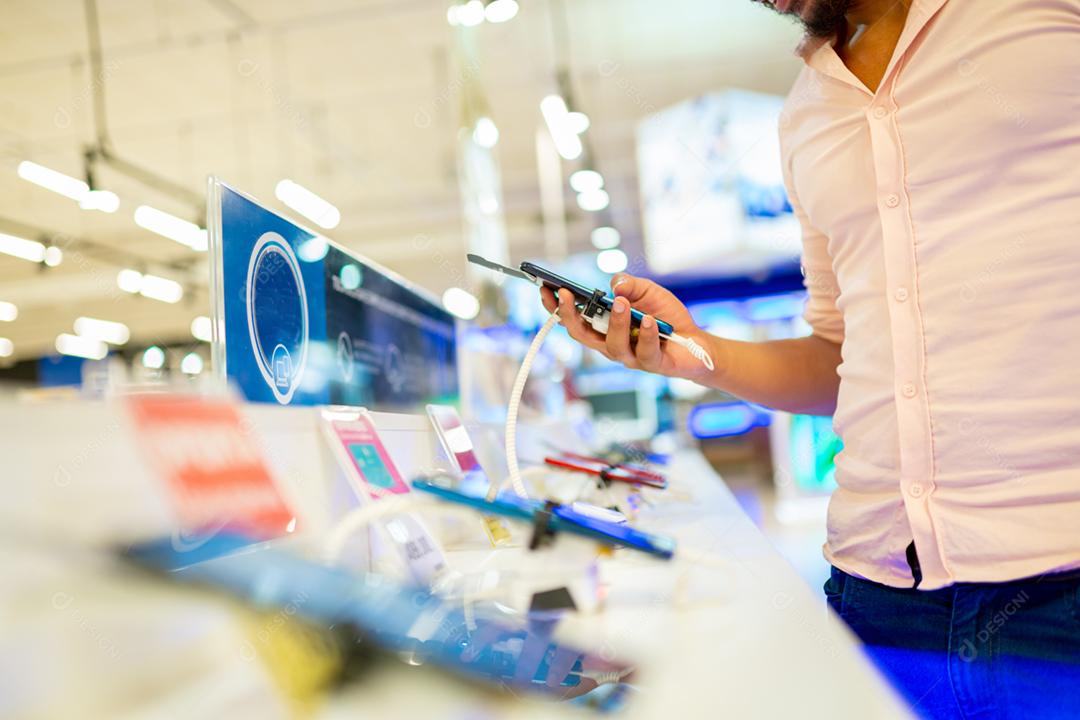 Homem latino-americano testando novos telefones no supermercado, foco na mão