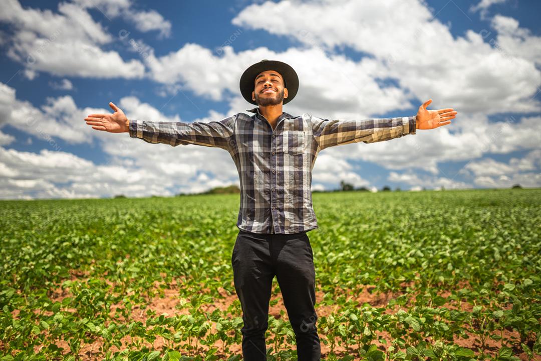 Feliz jovem agricultor latino-americano desfrutando de liberdade com as mãos abertas na fazenda