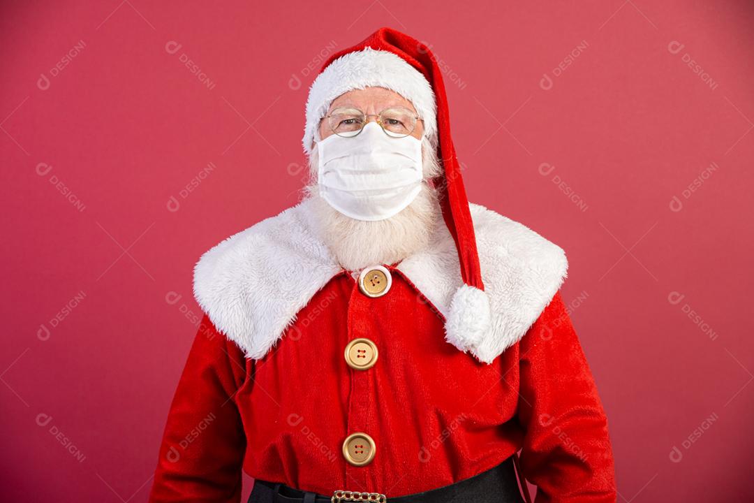 Verdadeiro Papai Noel com fundo vermelho, usando uma máscara protetora, óculos e chapéu. Natal com distanciamento social. Covid-19