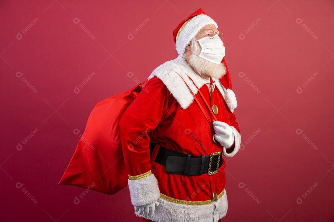 Verdadeiro Papai Noel em fundo vermelho, usando máscara protetora e com a mão aberta na frente