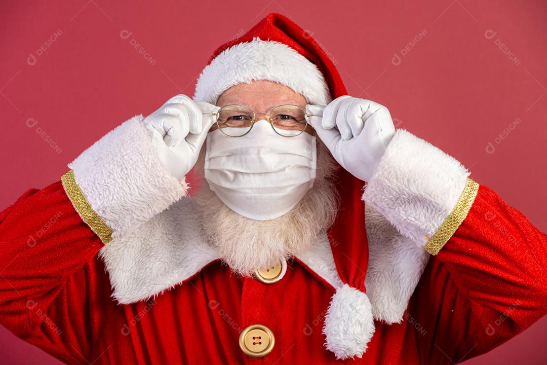 Verdadeiro Papai Noel com fundo vermelho, usando uma máscara protetora, óculos e chapéu. Natal com distanciamento social. Covid-19