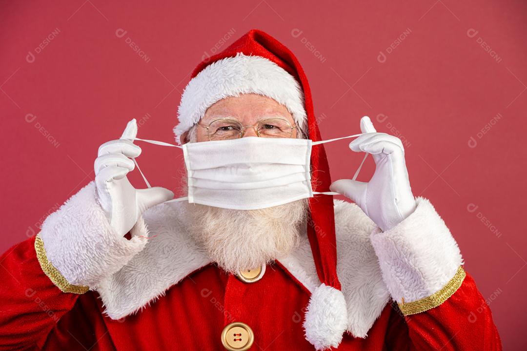 Verdadeiro Papai Noel com fundo vermelho, usando uma máscara protetora, óculos e chapéu. Natal com distanciamento social. Covid-19