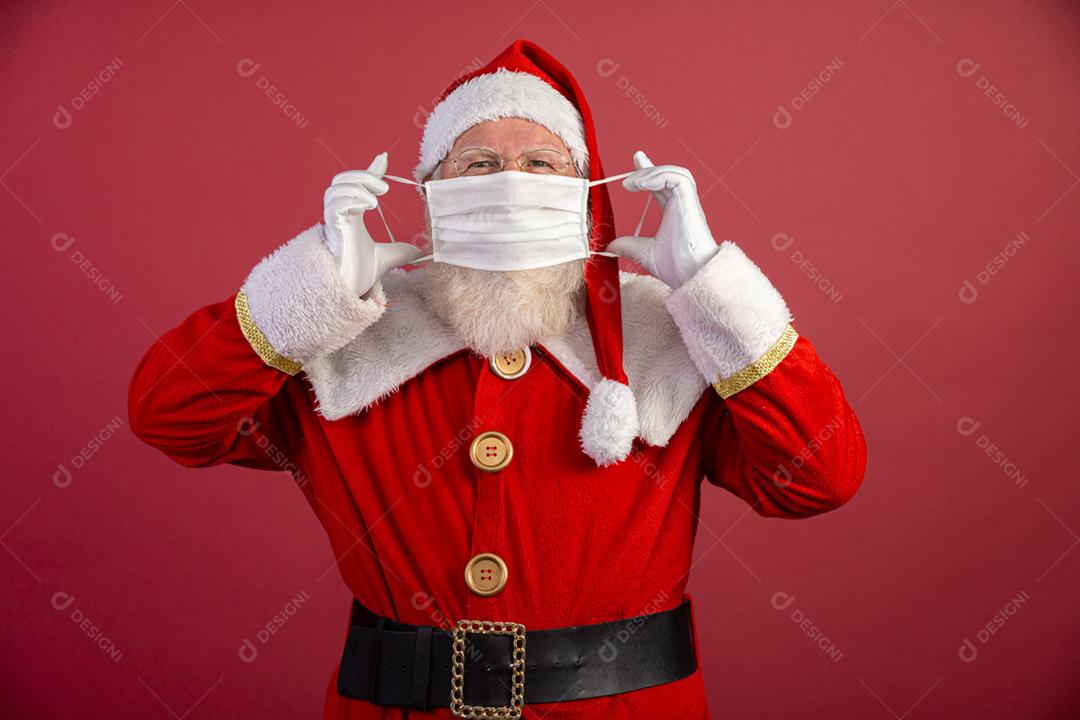 Verdadeiro Papai Noel com fundo vermelho, usando uma máscara protetora, óculos e chapéu. Natal com distanciamento social. Covid-19