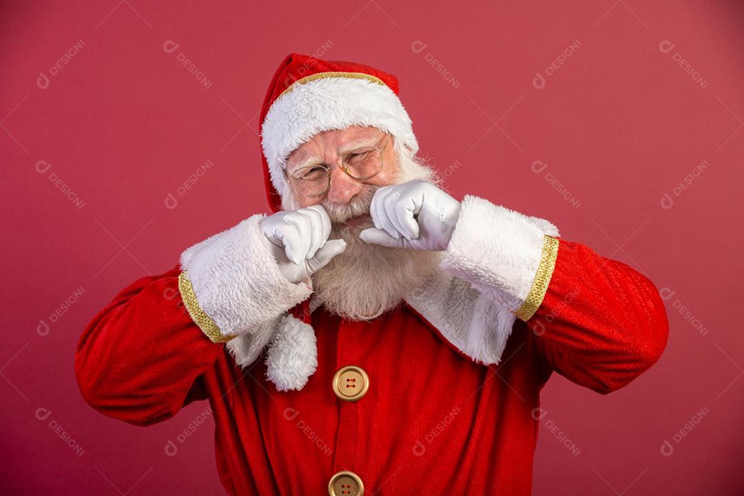 Papai Noel chorando em fundo vermelho, usando óculos e chapéu.