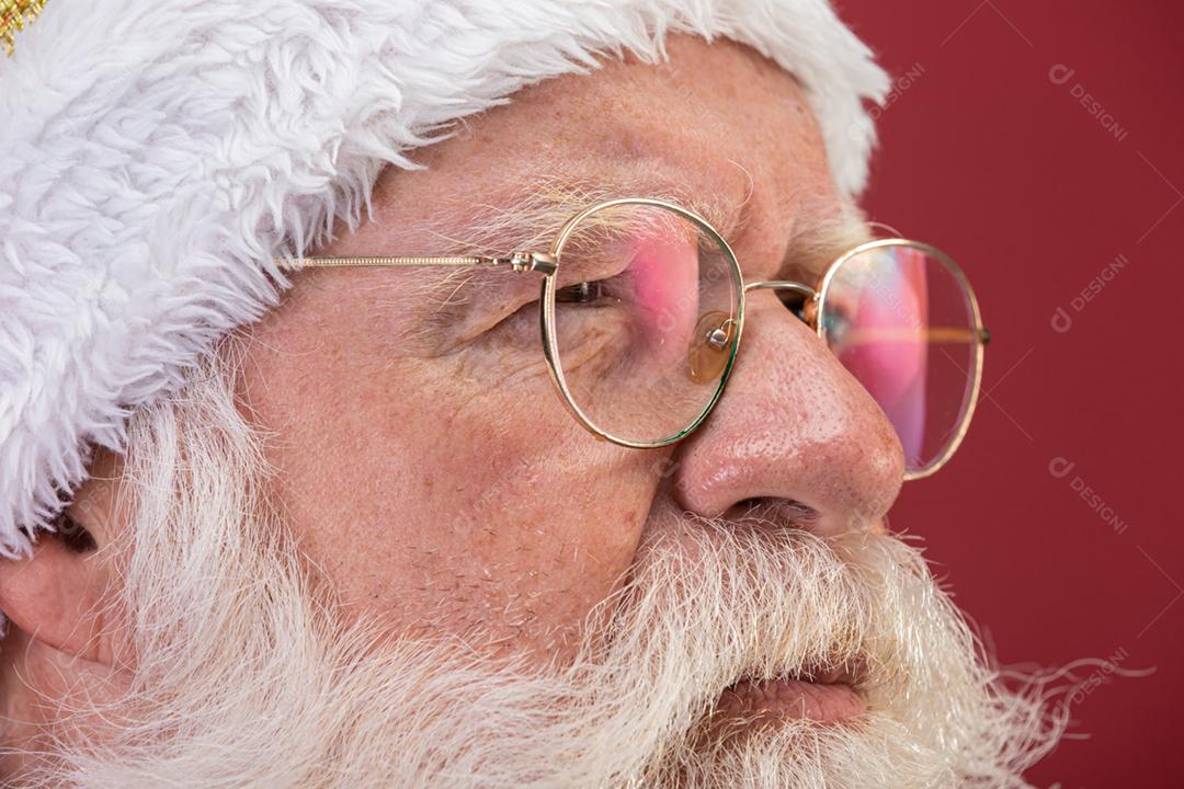 Verdadeiro Papai Noel com um fundo vermelho, usando óculos, luvas e um chapéu olhando de lado