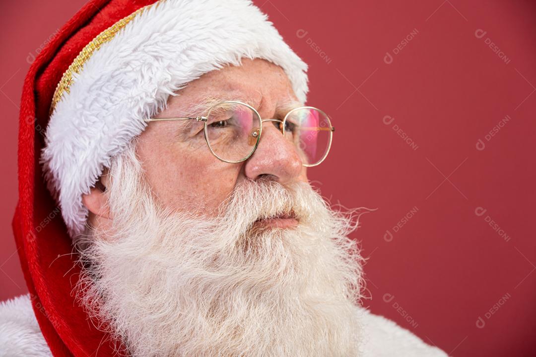 Verdadeiro Papai Noel com um fundo vermelho, usando óculos, luvas e um chapéu olhando de lado